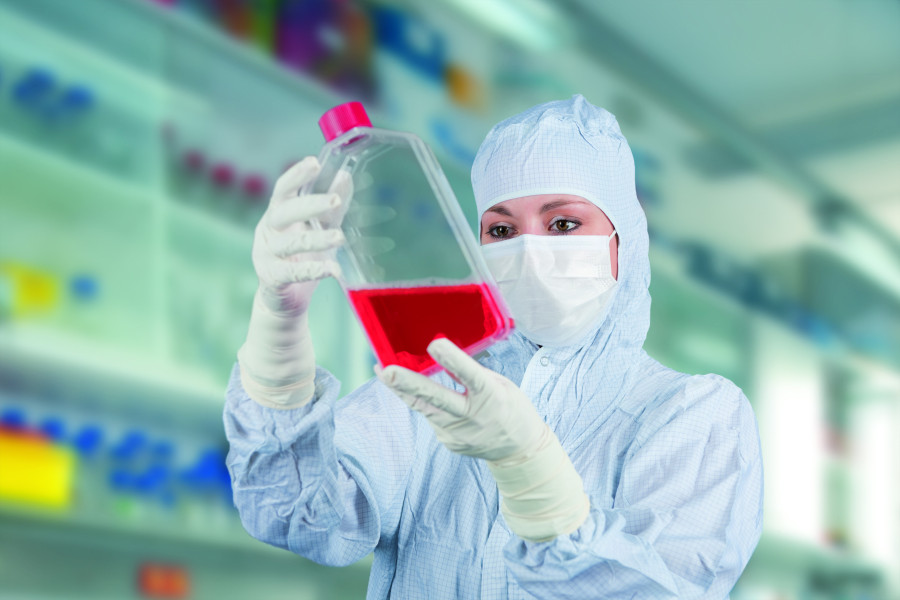 Wissenschaftlerin in Schutzkleidung beobachtet eine rote Flüssigkeit im Behälter