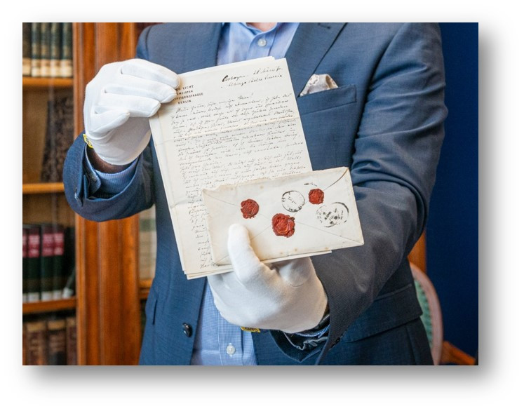 Mit weißen Handschuhen wird ein historischer Brief gerzeigt.