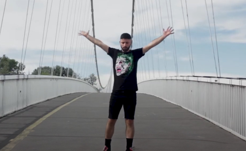 Ein junger Man in Shorts und T-Shirt steht mit augebreiteten Armen auf einer Hängebrücke.